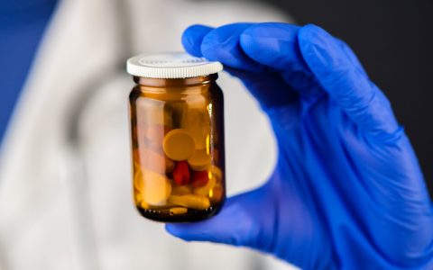 Female doctor holding unlabeled bottle of various pills and medication, prescription medicine and healthcare, selective focus