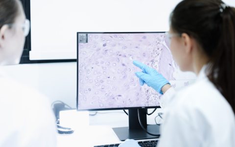 A pharmaceutical Quality Control QC team ensures GxP compliance. Two scientists review an electronic batch record on a tablet while a third performs a required analytical test.