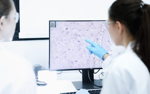 A pharmaceutical Quality Control QC team ensures GxP compliance. Two scientists review an electronic batch record on a tablet while a third performs a required analytical test.